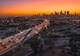 A four-lane bridge with arches stands above a Los Angeles highway. The city of LA is in the background, along with an orange sky. 