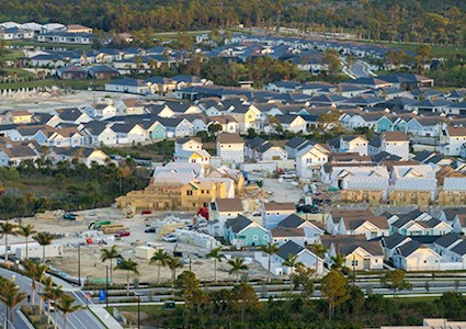 Aerial view of housing development with finished and unfinished homes and highway on lower left of image