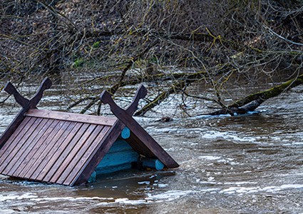 A small wooden structure partially submerged by river flooding with only its peaked roof visible.
