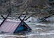 A small wooden structure partially submerged by river flooding with only its peaked roof visible.