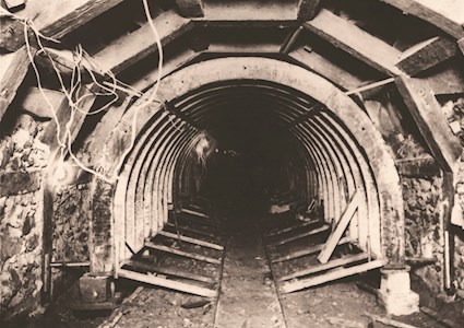 Sepia-toned photograph shows a tunnel being built with its timber supports. 