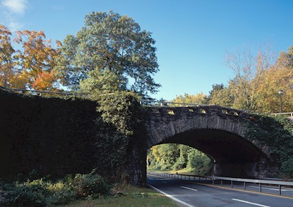 Image shows a four-lane parkway. Autumn-colored trees dot the landscape in the background. 