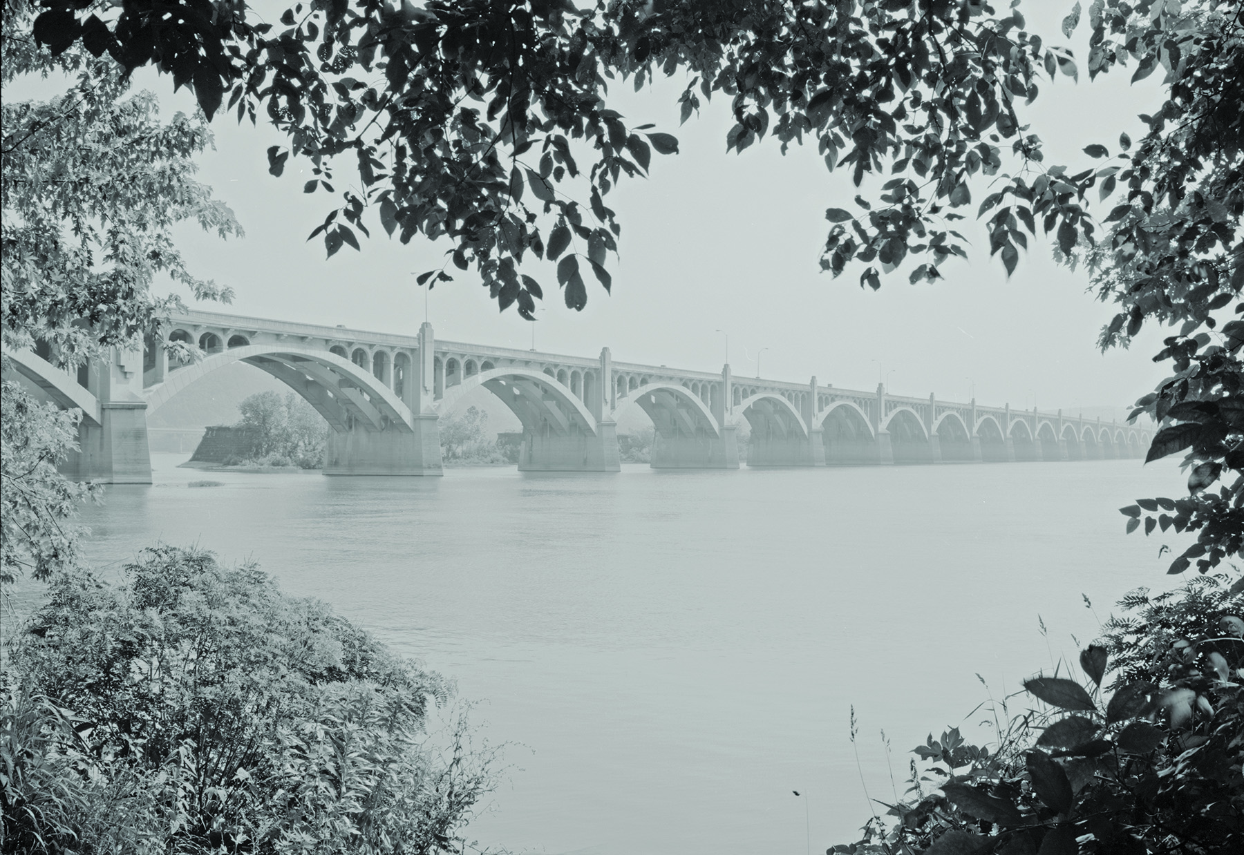 Black and white photo of a bridge over water that has many arches. 
