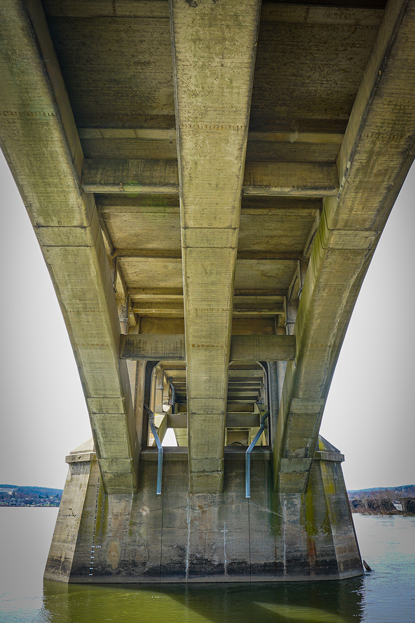 Photograph shows the underside of a bridge span. You can see three concrete arches. 