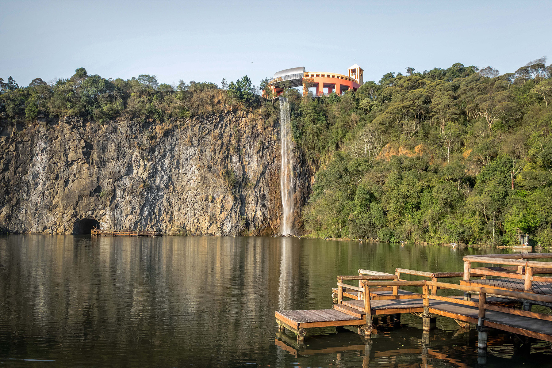 A lake is shown with a cliff face and waterfall in the background and a wooden deck in the foreground. 