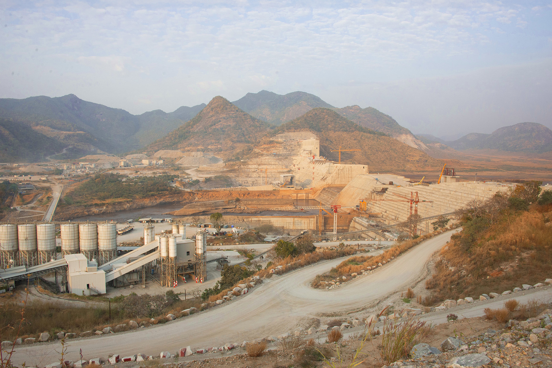 The photograph shows the massive dam under construction in an arid landscape. 