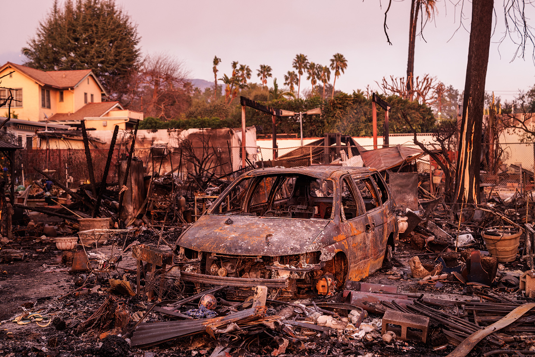 A burned-out car sits among other fire debris. 
