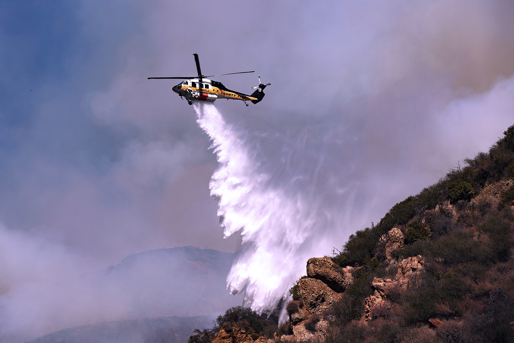 A helicopter dumps water on a Los Angeles area hillside.