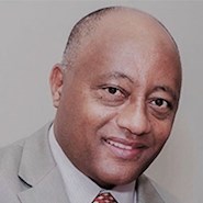 Man with brown skin in suit and tie smiles at the camera.