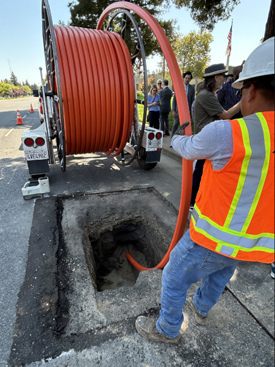 worker in orange vest and hardhat unspools tubing from a trailer