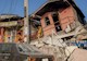 a man sits on the ground amid earthquake-damaged buildings