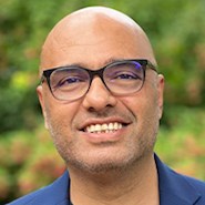 Man with glasses and dark blue Oxford shirt smiles at the camera.