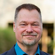 man in blue shirt and jacket smiles at the camera