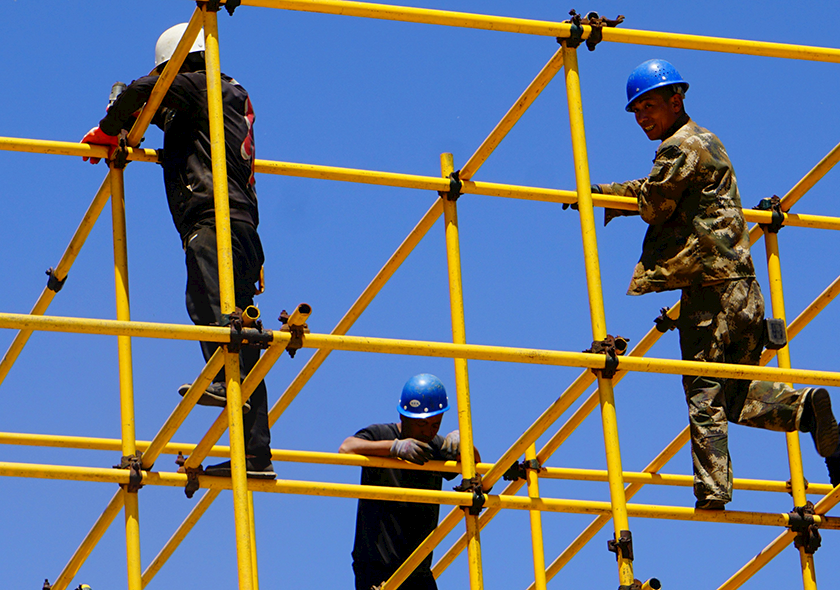 Men standing on support beams with hard hats